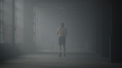 Muscular man doing cardio workout in loft building. Guy running in corridor