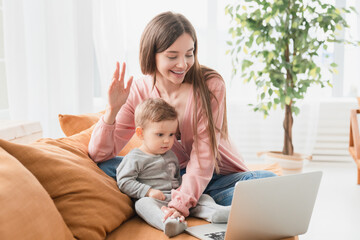 Happy young mother with toddler infant newborn baby having video call online conference...