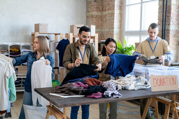 Intercultural people choosing donation clothes in volunteering office - Powered by Adobe