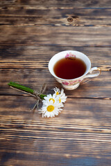 Cup of chamomile tea and chamomile flowers on wooden background. Close-up.