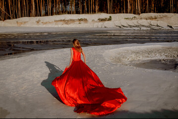 a girl in a red, long dress runs along the river bank.