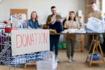Shopping cart with donation clothes against row of volunteers standing by table