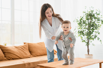 Young single mother teaching her little son toddler baby infant how to walk, crawling on the table,...