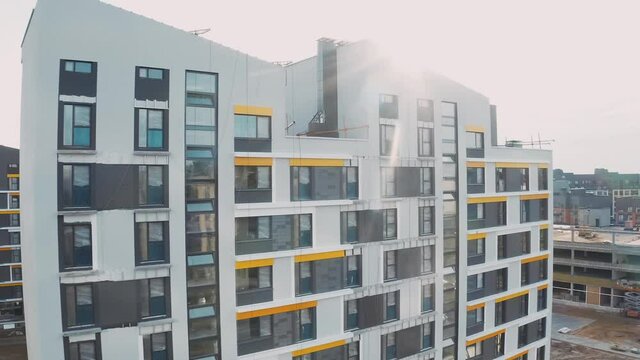 Construction site, building work process modern an apartment panel house. Unfinished structure city block of flats with courtyard, facade with windows and mansard roofs, aerial top view