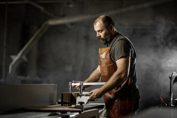 Brutal master carpenter saws wood blanks on machine in workshop
