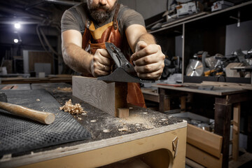 Close up master carpenter in an apron planes tree with a plane in workshop