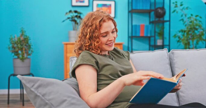 A mom-to-be relaxes on the couch during her maternity leave. She spends her free afternoon reading a book, a guide for moms-to-be on raising children, laughing, scoffing at the book