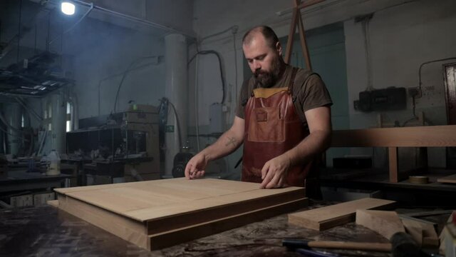 Brutal master carpenter prepares wooden blanks for work in workshop. High quality FullHD footage