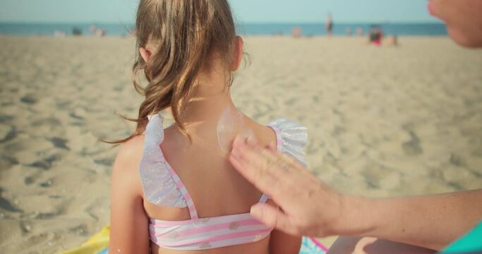 Mother applies sunscreen lotion on her daughter's back and skin to protect her from the sun a little girl is preparing to swim in the sea and play on the beach with her mother, using sunscreen, taking