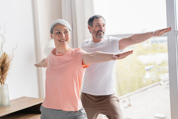 Fit sporty mature couple family spouses training stretching doing yoga exercises at home on lockdown. Middle-aged wife and husband doing sport together