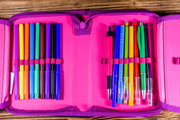 Different school stationeries (pens, pencils and felt tip pens) in a pink pencil box. Top view