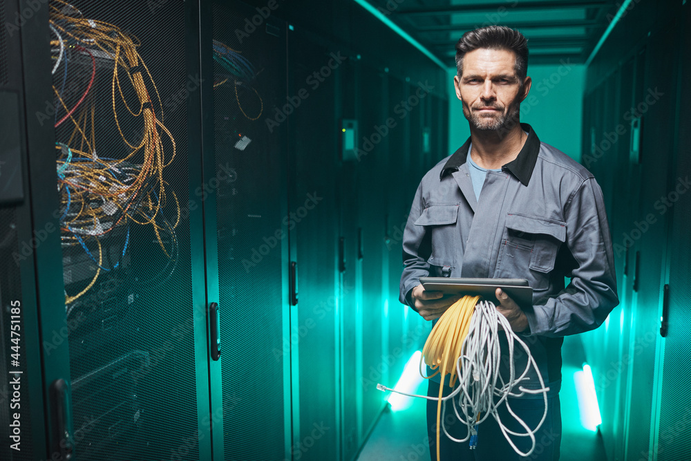 Wall mural waist up portrait of mature network engineer looking at camera and using digital tablet in server ro