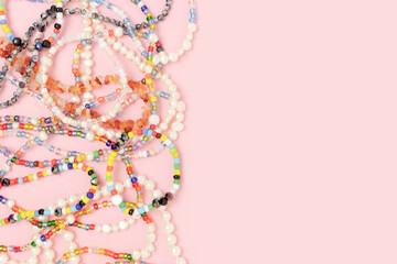Necklaces and bracelets made from beads and pearls on a pink pastel background with copyspace.