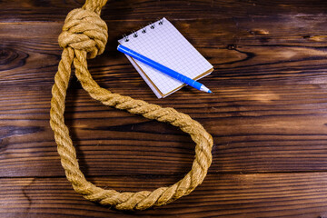 Rope with noose for the suicide, blank notepad and pen on wooden background