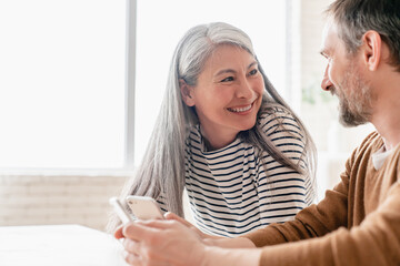 Smiling happy middle-aged mature couple family wife and husband woman and man using smart phones...