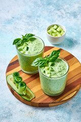 Cucumber Gazpacho - cold summer soup with basil in glasses on wooden board on light background