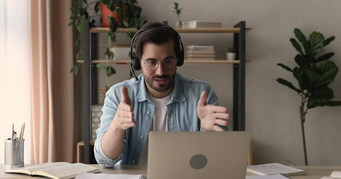 Smart young man in eyeglasses wearing wireless headphones with microphone, holding video call conversation using web camera zoom software application on computer, discussing working issues distantly.