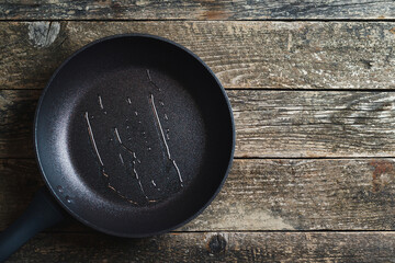 Empty fry pan over wooden background. Top view, copy space. Dark grey culinary background.