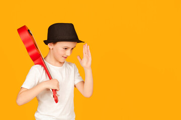 Fashionable boy in summer hat isolated over orange background. Little boy plays on hawaiian guitar and having fun.