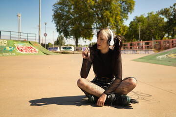 Cute young girl with heterochromia and punk style with white headphones and inline skates sitting...