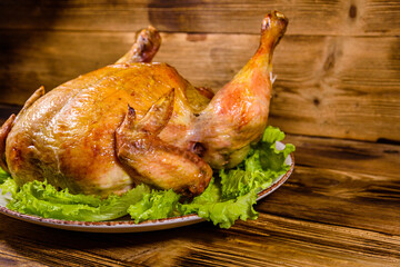 Plate with roasted whole chicken and lettuce leaves on a wooden table