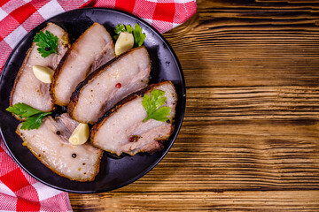 Slices of baked pork belly, garlic and parsley on a black plate. Top view