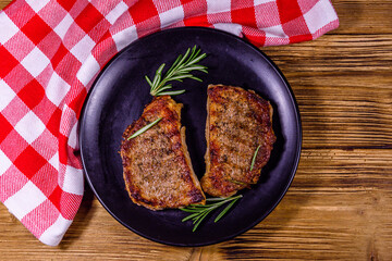 Plate with roasted steaks and rosemary twigs on a wooden table. Top view