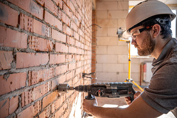 A builder in a helmet and goggles works with a drill.