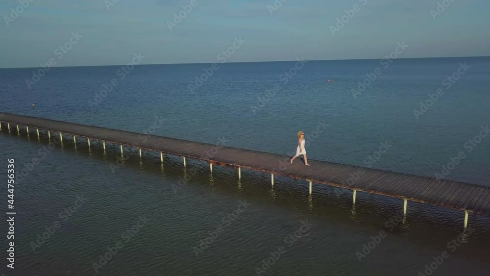 Poster a girl walks on a wooden pier near the sea