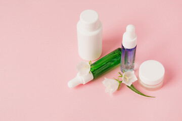 Cosmetics bottle with beauty product and wild plants on pink background. Natural skin and hair care. Wellbeing concept. Copy space