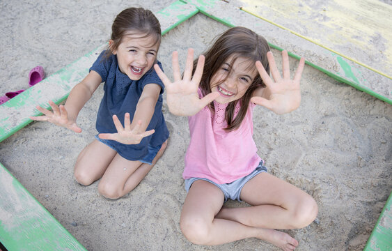 Funny little girls play with sand in the sandbox.