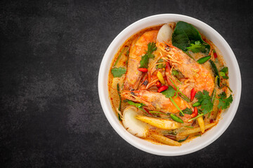 Tom Yum Goong, Tom Yum Kung, Thai food, hot and sour shrimp soup, creamy style in white ceramic bowl on dark tone texture background with copy space for text, top view