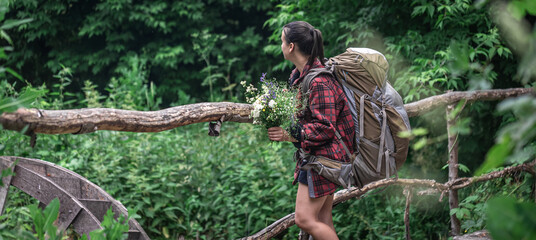 Naklejka na ściany i meble A girl on a hike in the woods with a large tourist backpack.
