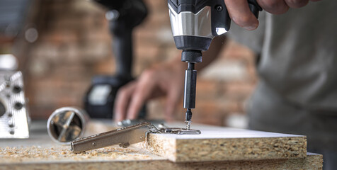 A man is screwing in a screw, a self-tapping screw for wood.