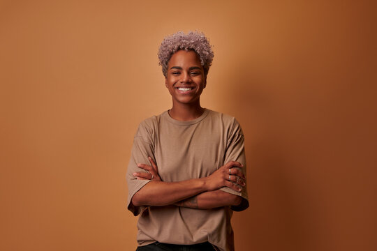 Head shot portrait smart confident smiling millennial African American woman standing with folded arms over beige wall. Attractive young biracial teenager student girl freelancer looking at camera.