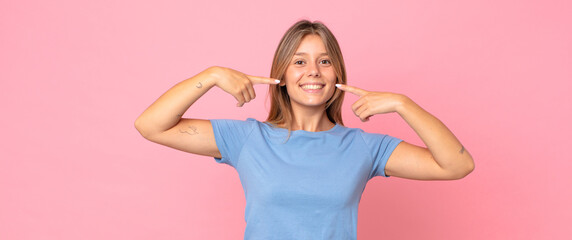 blonde pretty woman smiling confidently pointing to own broad smile, positive, relaxed, satisfied...