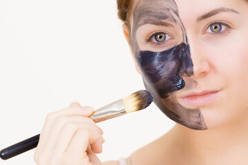 Female applying black mud facial mask