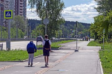 Two young men ride scooters on a bike path on a summer day