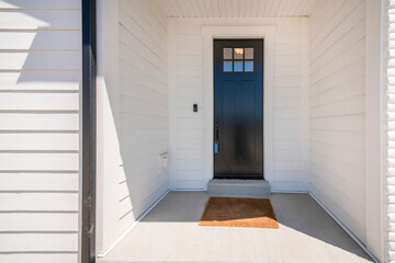 Exterior of a house with a view of black wooden door with glass panel and an enginered wood sidings