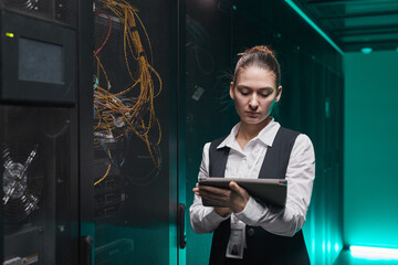 Waist up portrait of female network engineer using digital tablet while setting up servers in data center, copy space