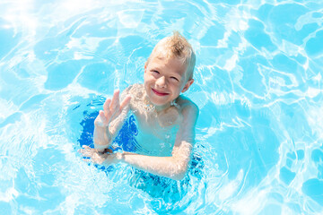 Fototapeta na wymiar happy baby boy swimming in the blue water pool, the concept of summer holidays and school holidays