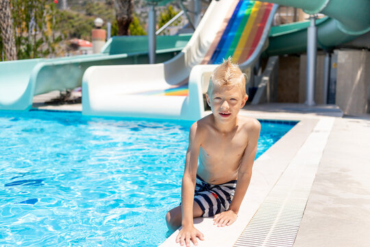 happy baby boy sitting by the pool with water slides, the concept of summer holidays at the sea and school holidays