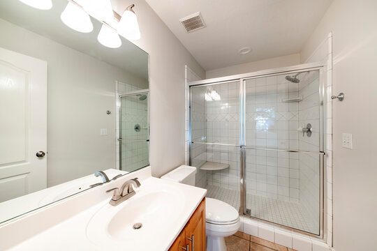 Interior of a bathroom with wooden vanity sink with tile counter and shower stall with glass