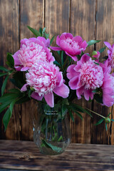 Peony and flower buds in a glass vase. A wooden wall in the background. Flowers on a wooden background.