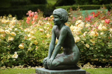 Small sculpture or statue of a little girl kneeling surrounded by plants and trees in the center of the Byparken, which is a pretty public park in the center of the city of Haugesund, Norway.