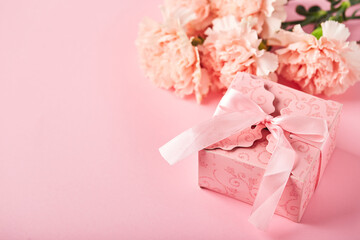 Bouquet of pink carnations and pink gift box. Design concept of holiday greeting with carnation bouquet on pink background