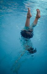 A child dips his head into the water, feet look out of the water.