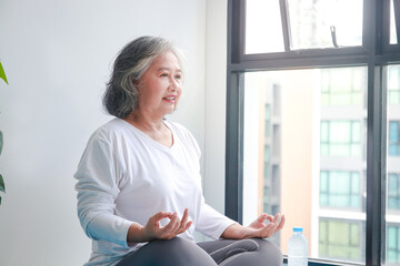 Asian elderly woman sitting at home exercising, doing yoga poses. Social distancing, exercise to...