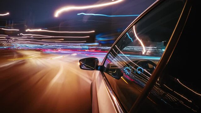 Motion timelapse of a speedy night drive in a big city ending in the underground car parking. Side view from the car window to the road with light trails from vehicles and street lights.