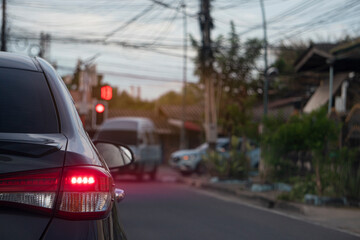 Rear side of gray car turn on brake light with motion of red light. Stop on asphalt road by traffic red  for background. Blurred another car turned left in the countryside.